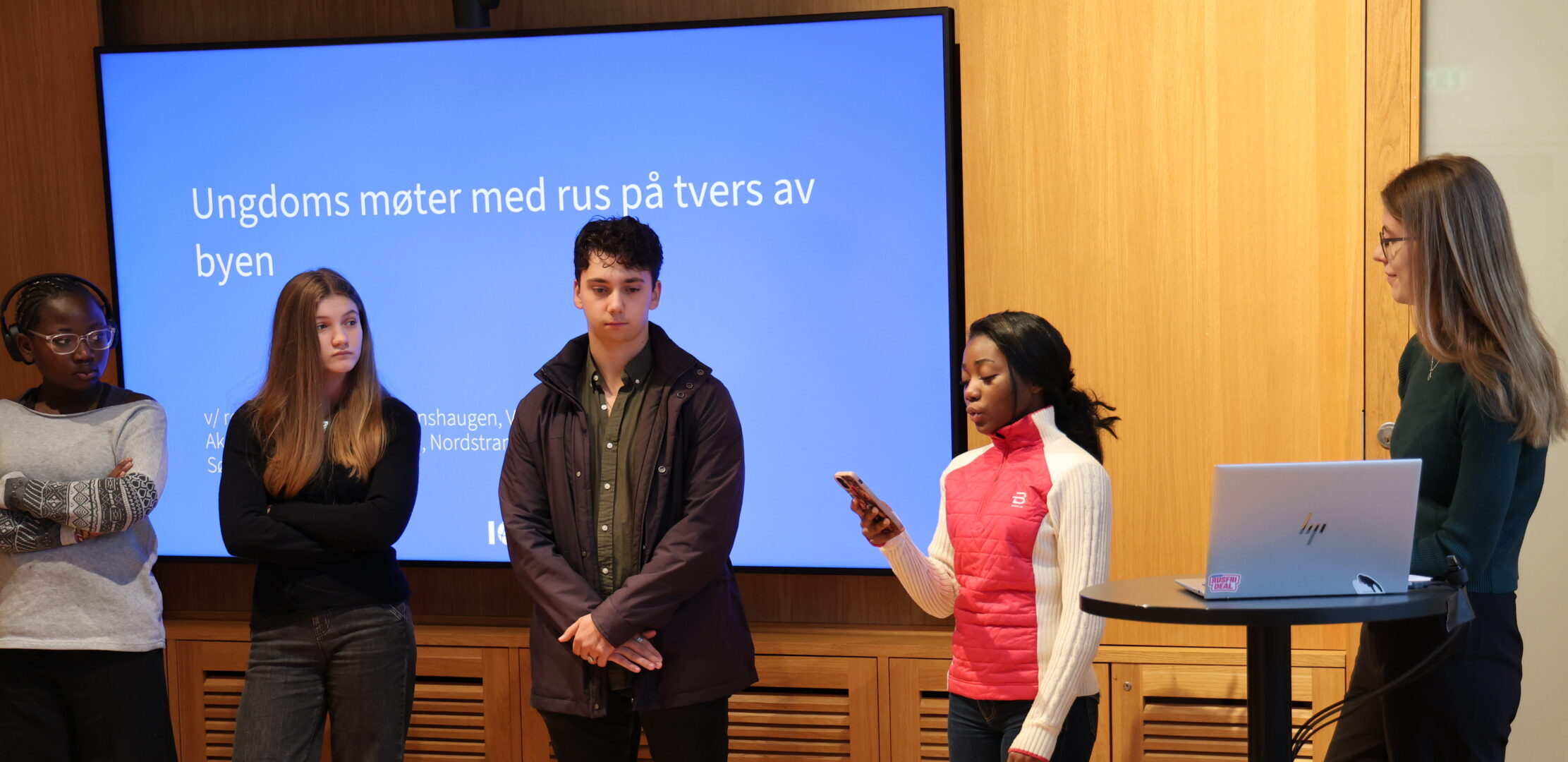 Ungdommer står foran presentasjon på en skjerm.