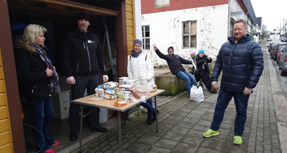 Ved et bord utenfor garasjen deler Jørn Hansen ut mat til smilende brukere som står på trygg avstand.